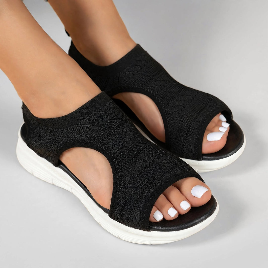 Black open toe knitted sandals with a white sole and black stitching.