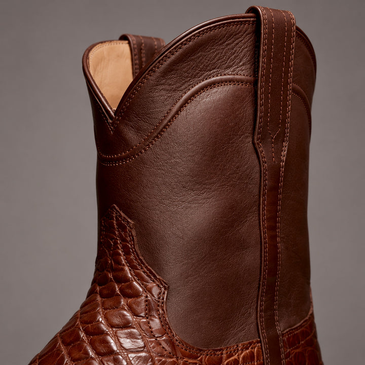 Dark brown mid-calf boots with matte upper and glossy reddish-brown reptile-pattern lower panel. (detail macro)