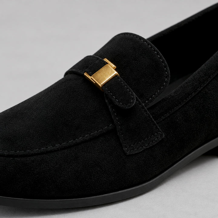 Matte black suede-look loafers with a black sole and gold buckle. (detail macro)