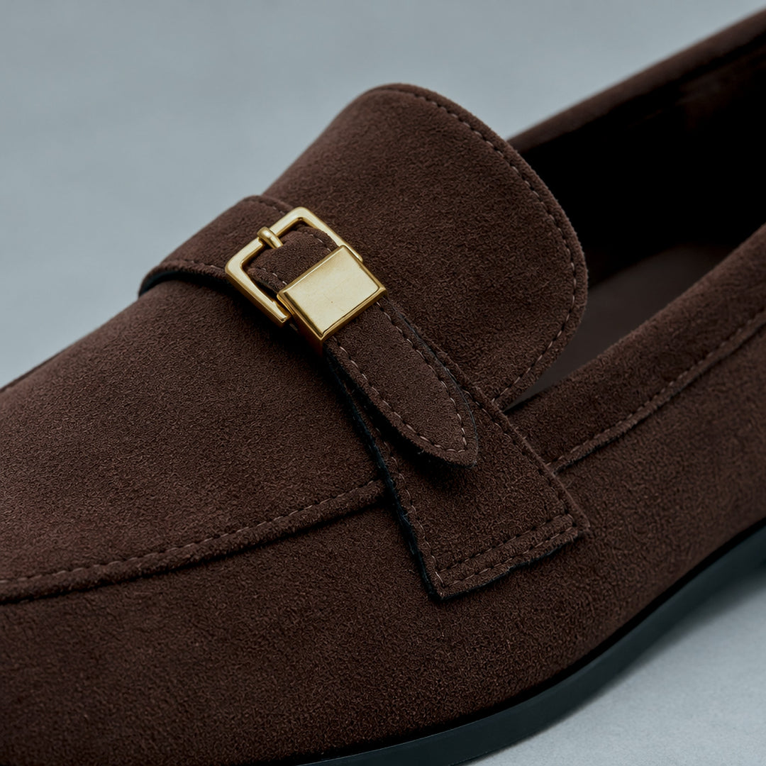 Matte dark brown suede-look loafers with a black sole and gold buckle. (detail macro)