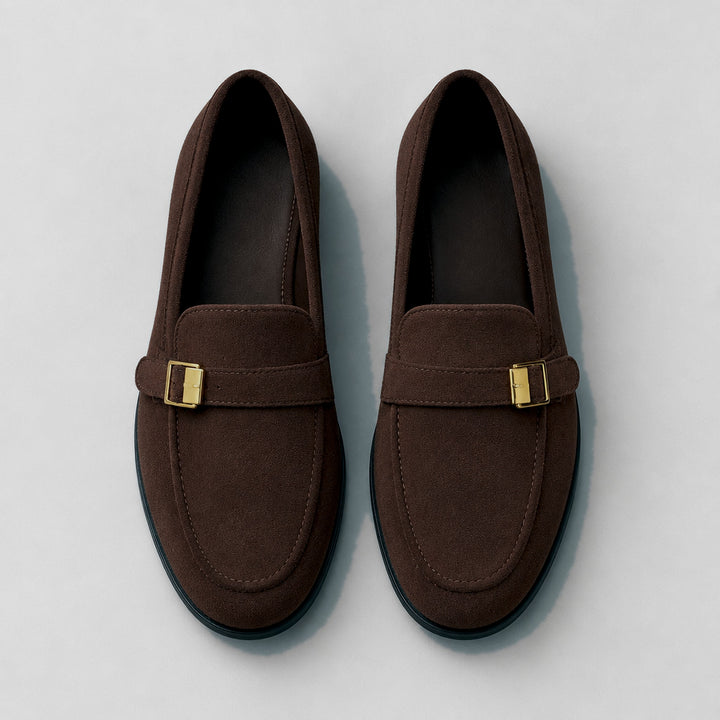 Matte dark brown suede-look loafers with a black sole and gold buckle. (top down)