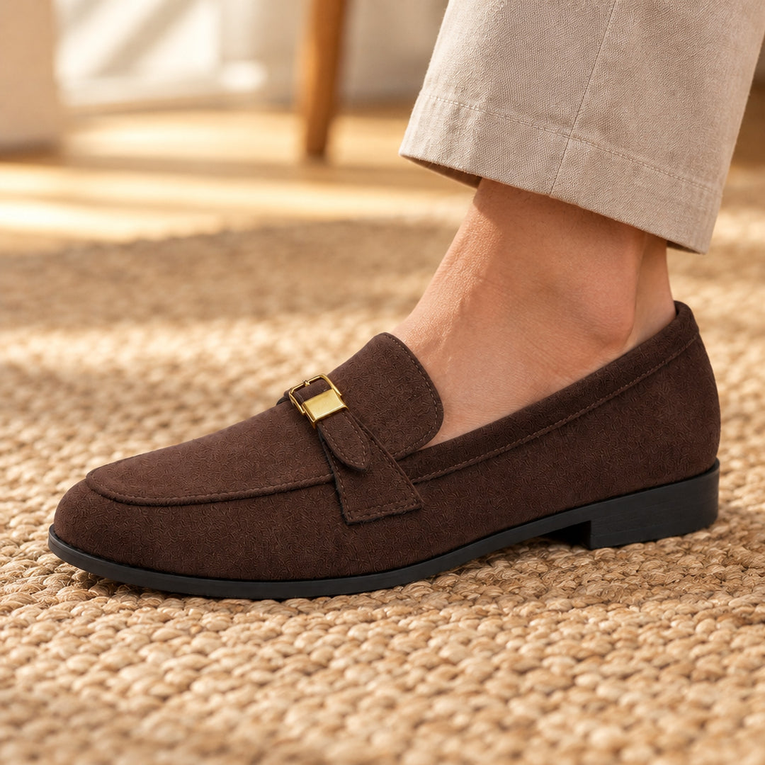 Matte dark brown suede-look loafers with a black sole and gold buckle. (on model lifestyle)
